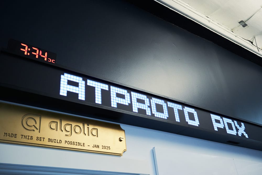 A dot-matrix LED sign reading "ATPROTO PDX" above a brass plaque: "Algolia made this set build possible — Jan 2025." A red LED clock in the corner frozen at 3:34:25.