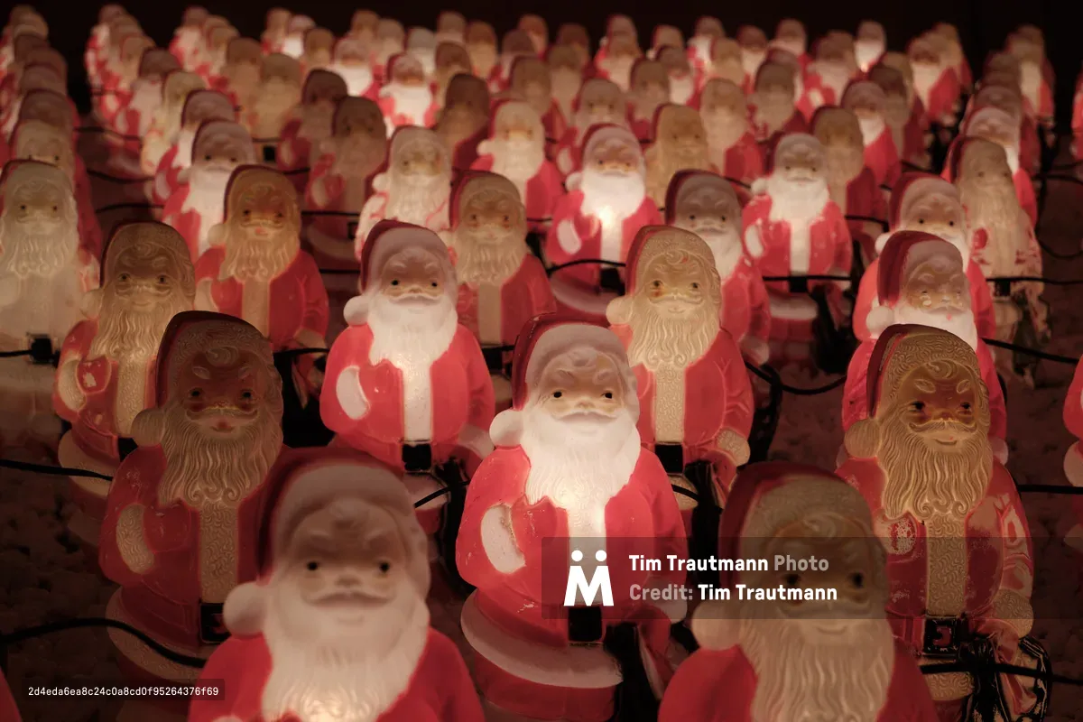 Hundreds of plastic Santa Claus figurines create a mesmerizing sea of red and white beneath the glow of string lights in Portland's Concordia neighborhood. The illuminated collection stretches into darkness, each jolly figure casting gentle shadows while warm light emanates from within their translucent forms. This enchanting holiday installation transforms an ordinary urban space into a whimsical wonderland, where countless identical Santas stand in silent formation like a benevolent Christmas militia.