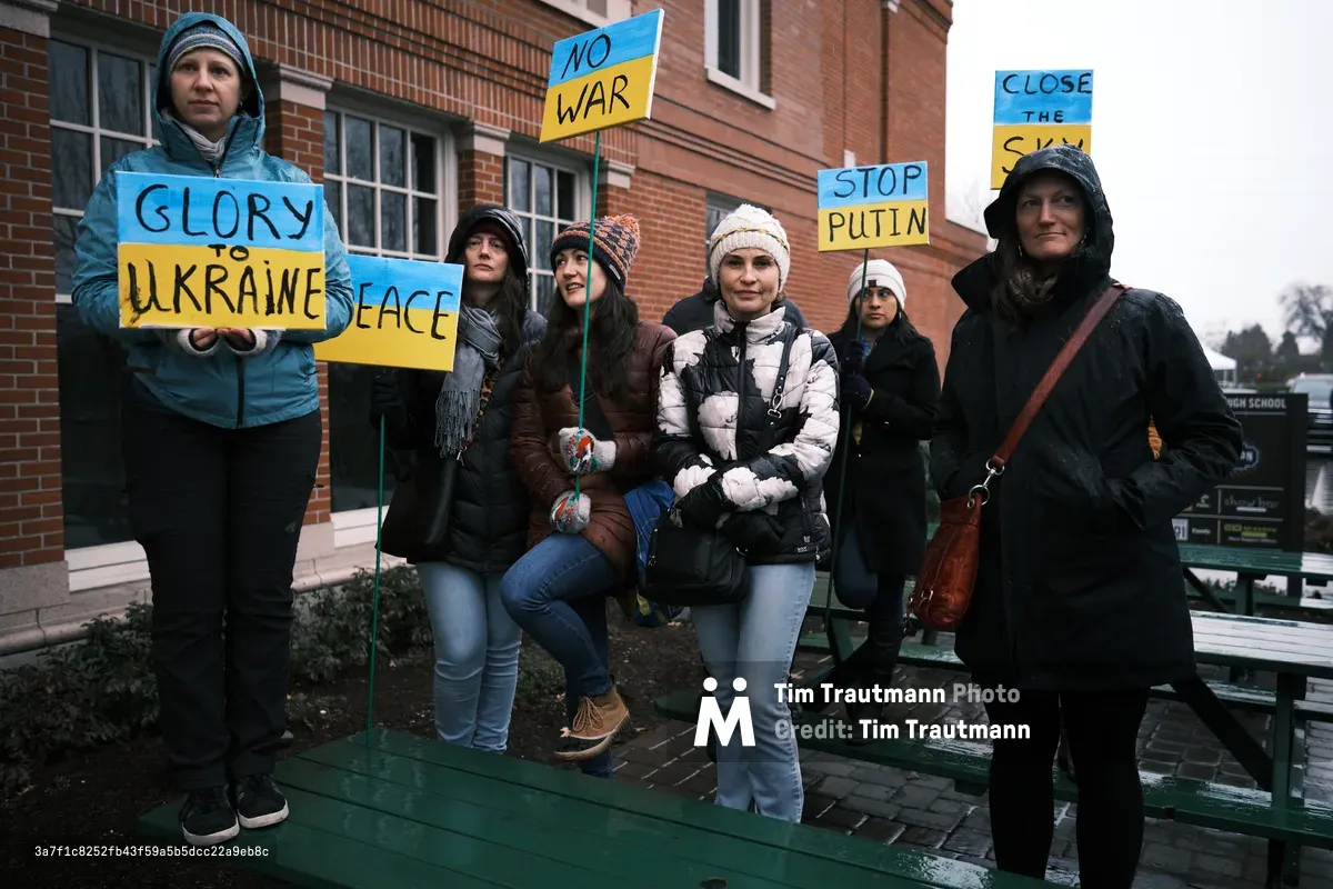 A determined group of protesters gather on the rain-slicked steps of Portland's Revolution Hall, their handmade signs bearing urgent messages of support for Ukraine and opposition to Putin's aggression. Bundled against the Pacific Northwest chill in puffy jackets and knit beanies, the demonstrators create a tableau of quiet resolve, their blue and yellow signs echoing Ukraine's national colors. The overcast winter light casts a somber mood over the scene, while the brick facade of the historic venue provides a stately backdrop to this moment of civic engagement captured just days before Russia's invasion would make their prescient warnings tragically relevant.