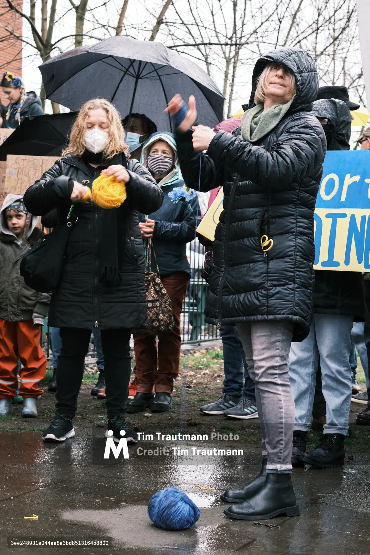Bundled against Portland's winter chill, protesters gather outside Revolution Hall in the Central Eastside, their breath visible in the cold air as they demonstrate against the looming threat of war in Ukraine. Rain-slicked pavement reflects the gray afternoon light while masked demonstrators clutch signs and umbrellas, embodying both vulnerability and determination. The scene captures the prescient urgency of citizens mobilizing days before Russian hostilities would transform their fears into reality.