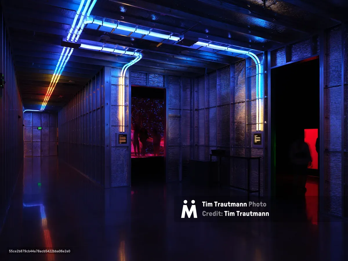 A modern gallery interior at Hopscotch in Portland, Oregon featuring dramatic blue and red neon lighting strips running along the ceiling and walls, creating a sci-fi atmosphere with reflective floors and industrial architecture.
