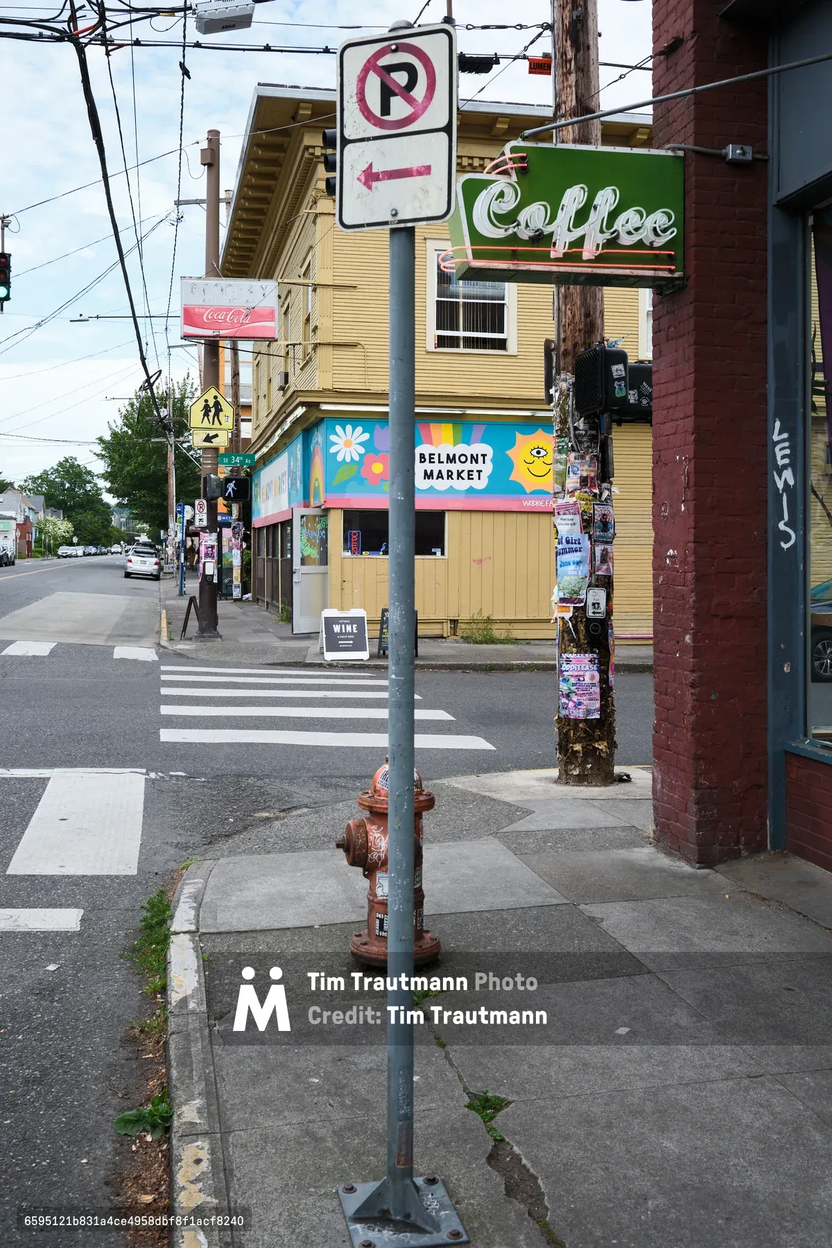 A street corner view in Portland, Oregon showing a crosswalk, no right turn sign, fire hydrant, and local businesses including Belmont Market and a coffee shop. The scene captures the eclectic urban character of the Belmont district with colorful storefronts, utility poles, and mixed-use buildings.