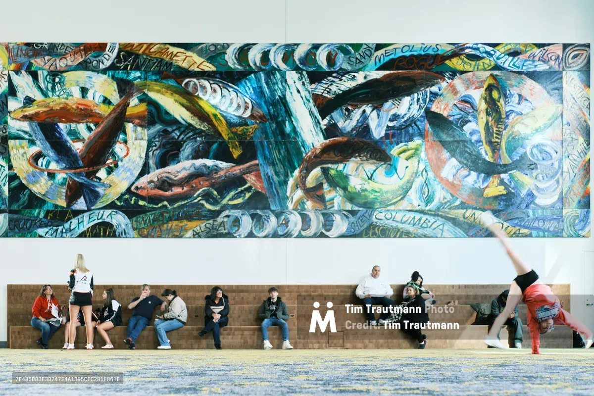 Visitors seek momentary refuge on stone benches beneath an explosive panorama of maritime-themed murals at Portland's Oregon Convention Center. The vibrant wall art, dominated by swirling blues and oceanic motifs interwoven with text fragments, creates a dramatic backdrop for the diverse group of attendees—from a breakdancer frozen mid-move to couples and individuals in casual repose. The juxtaposition of kinetic street art energy above and human stillness below captures the convention center's role as both cultural crossroads and temporary sanctuary.