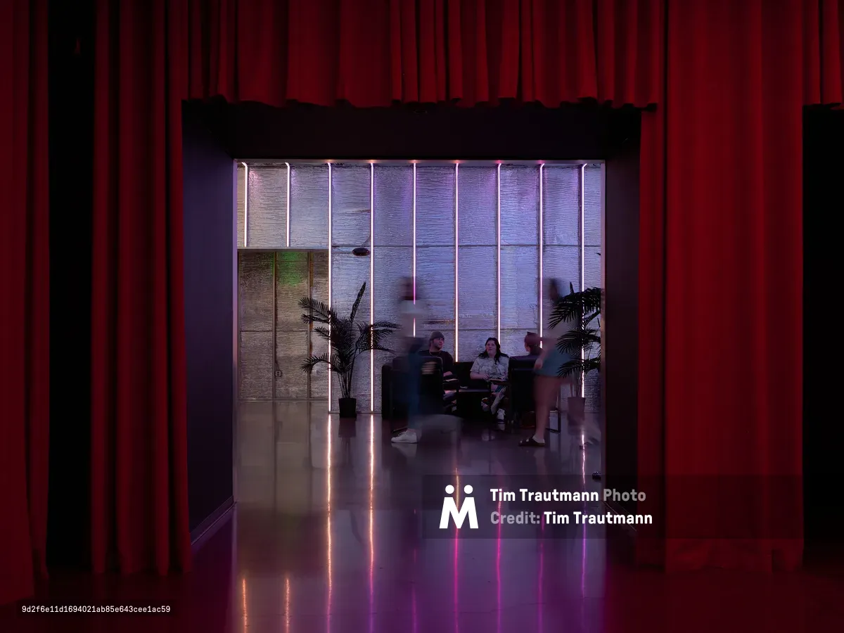 A contemporary restaurant interior at Hopscotch in Portland, Oregon featuring dramatic red curtains framing the entrance, purple and pink neon tube lighting, polished concrete floors with colorful reflections, and diners seated at tables in the background with decorative palm plants.