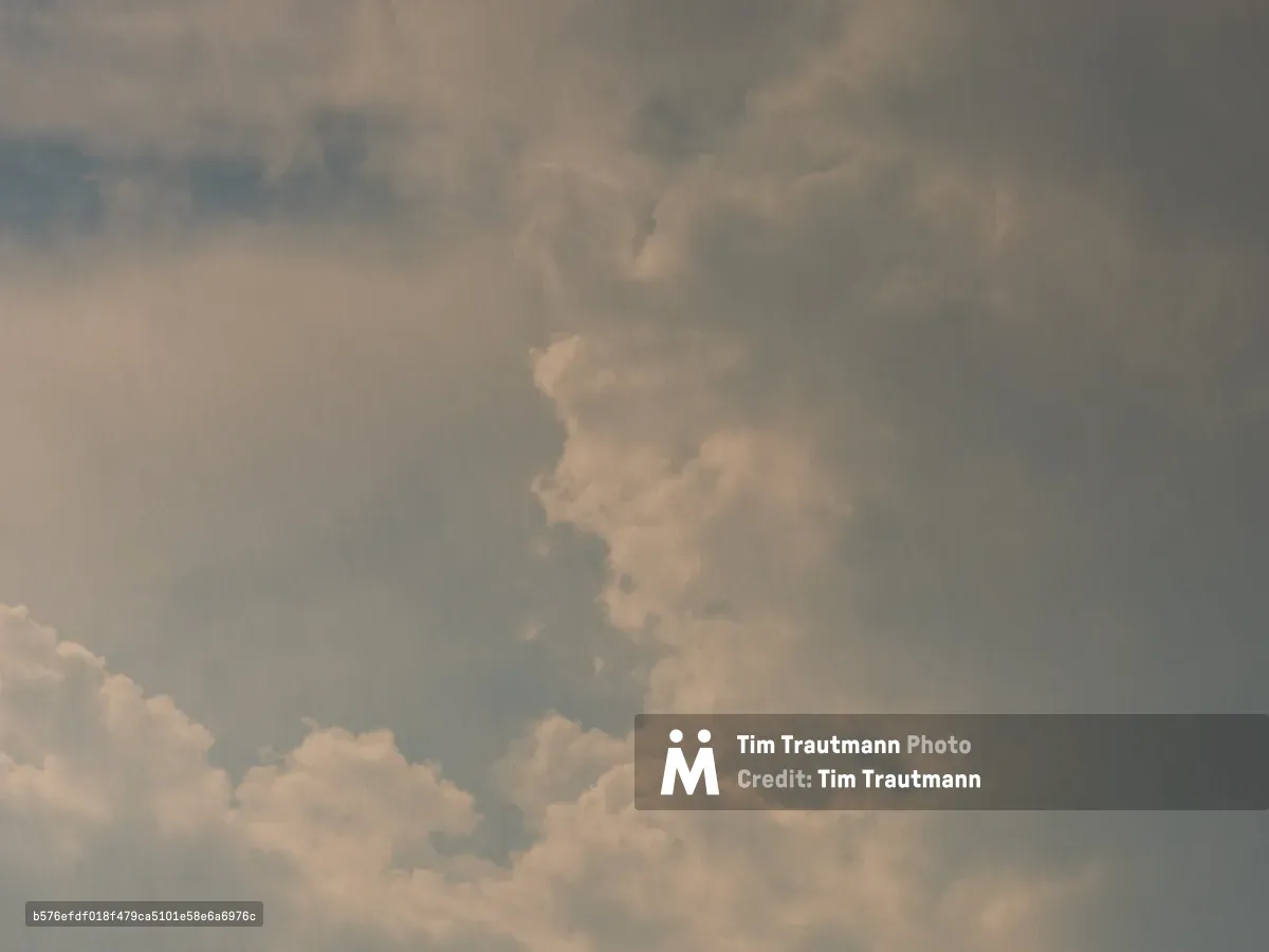 A moody sky filled with thick, billowing clouds in various shades of gray and white, captured over Portland, Oregon. The atmospheric conditions create a dramatic overcast scene with layers of cumulus clouds against a muted sky.