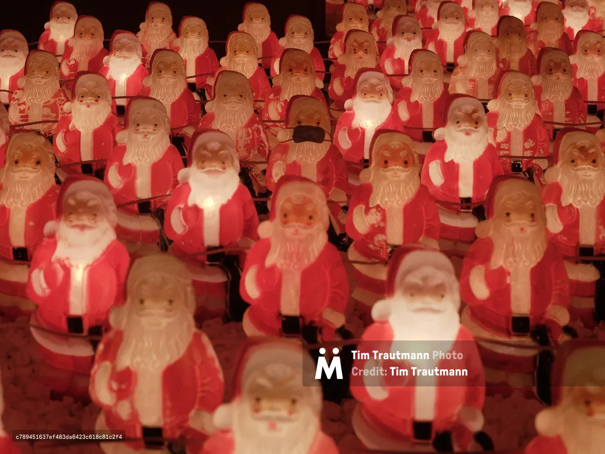 Dozens of molded plastic Santa Claus figures glow with warm amber light in Chris Willis's annual art installation at a Sellwood consignment gallery. The repetitive crimson-clad figures create a mesmerizing pattern that stretches into darkness, their identical jolly expressions caught between whimsy and unsettling uniformity. The installation transforms the humble Christmas decoration into a commentary on mass production and holiday commercialization, with each illuminated Santa casting a soft pool of light in the gallery's shadowy interior.