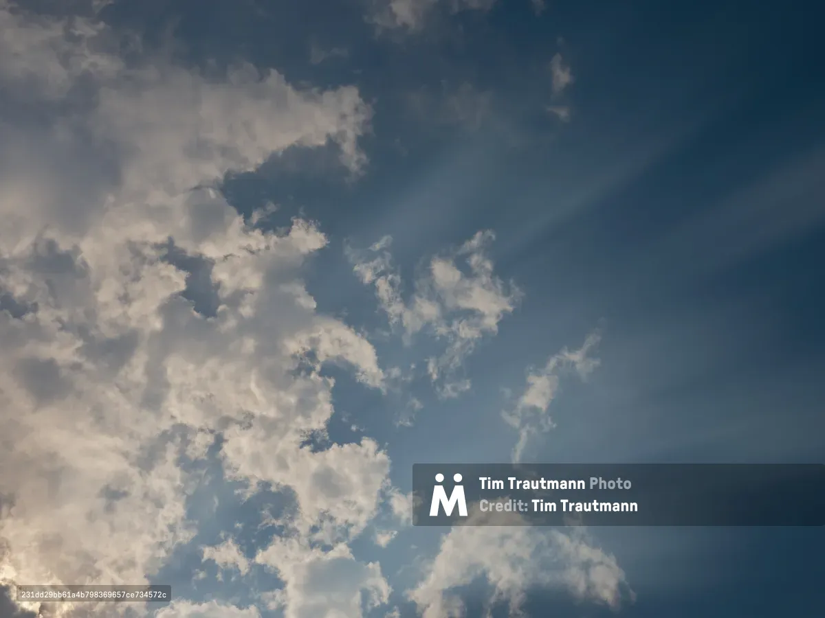 A dramatic sky filled with billowing white and gray clouds against a deep blue backdrop, captured over Portland, Oregon. The clouds show various textures and densities, creating a dynamic atmospheric scene with natural lighting variations.