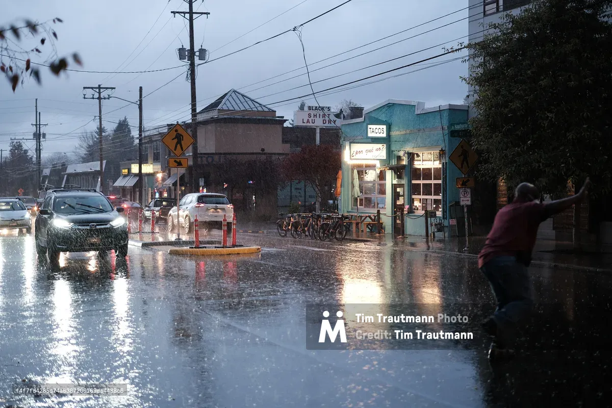A heavy rainstorm drenches the intersection of SE Hawthorne Boulevard and SE 47th Avenue in Portland, Oregon. The teal-painted exterior of the popular ¿Por Qué No? taqueria glows warmly on the right, with its "Tacos" sign illuminated and a row of bikeshare bicycles parked out front. A man in a red shirt dashes across the flooded intersection on the right, arms outstretched for balance. Car headlights reflect off the standing water on the street as traffic backs up in the stormy blue-grey dusk. Black's Shirt Laundry is visible in the background.