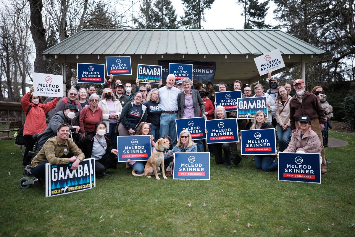A large group of political supporters gathered outdoors in Oregon City, Oregon, holding campaign signs for McLeod Skinner and Gamba candidates. The diverse group of approximately 30-40 people poses in front of a covered pavilion structure, with many wearing casual outdoor clothing and some face masks, creating an energetic grassroots campaign atmosphere.