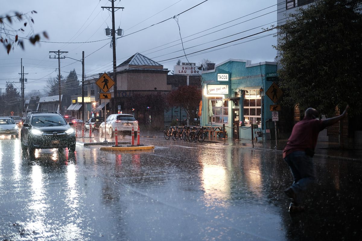 A heavy rainstorm drenches the intersection of SE Hawthorne Boulevard and SE 47th Avenue in Portland, Oregon. The teal-painted exterior of the popular ¿Por Qué No? taqueria glows warmly on the right, with its "Tacos" sign illuminated and a row of bikeshare bicycles parked out front. A man in a red shirt dashes across the flooded intersection on the right, arms outstretched for balance. Car headlights reflect off the standing water on the street as traffic backs up in the stormy blue-grey dusk. Black's Shirt Laundry is visible in the background.