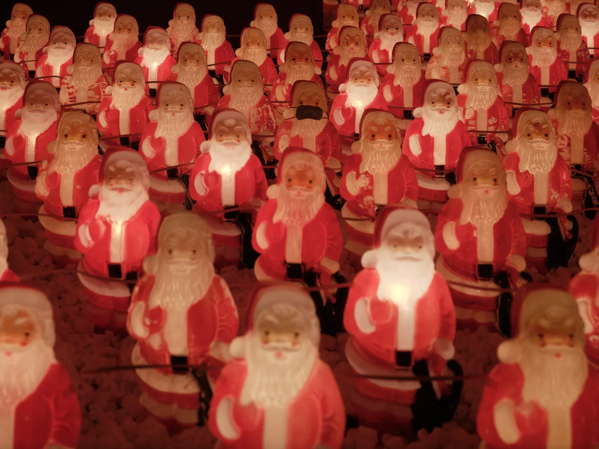 Dozens of identical illuminated Santa Claus figurines create a mesmerizing sea of red and white in Portland's Sellwood neighborhood. The glowing plastic figures, part of Chris Willis's annual art installation, cast warm amber light against the darkness, their repetitive forms suggesting both festive abundance and unsettling uniformity. Each Santa bears the same benevolent expression and raised hand gesture, creating a hypnotic pattern that stretches beyond the frame's edges.