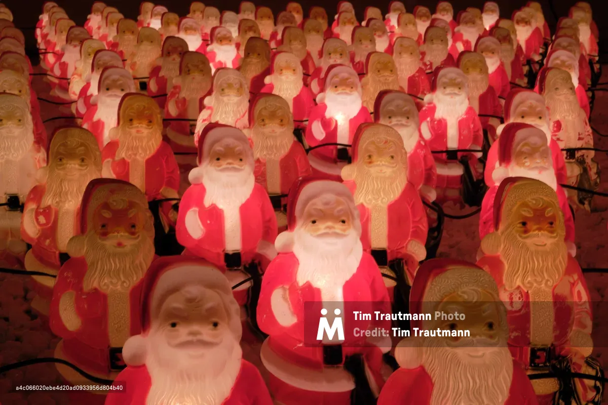 Hundreds of plastic Santa Claus figurines glow with warm amber light against the Portland night, creating an enchanting yet surreal holiday spectacle. The illuminated figures stretch endlessly into the darkness, their benevolent faces casting a golden warmth across Northeast Killingsworth Street. Black electrical cords snake between the jolly army, connecting each Santa in Chris Willis's whimsical annual Christmas installation. The repetitive nature of the identical figures transforms the familiar holiday icon into something both magical and slightly unsettling.