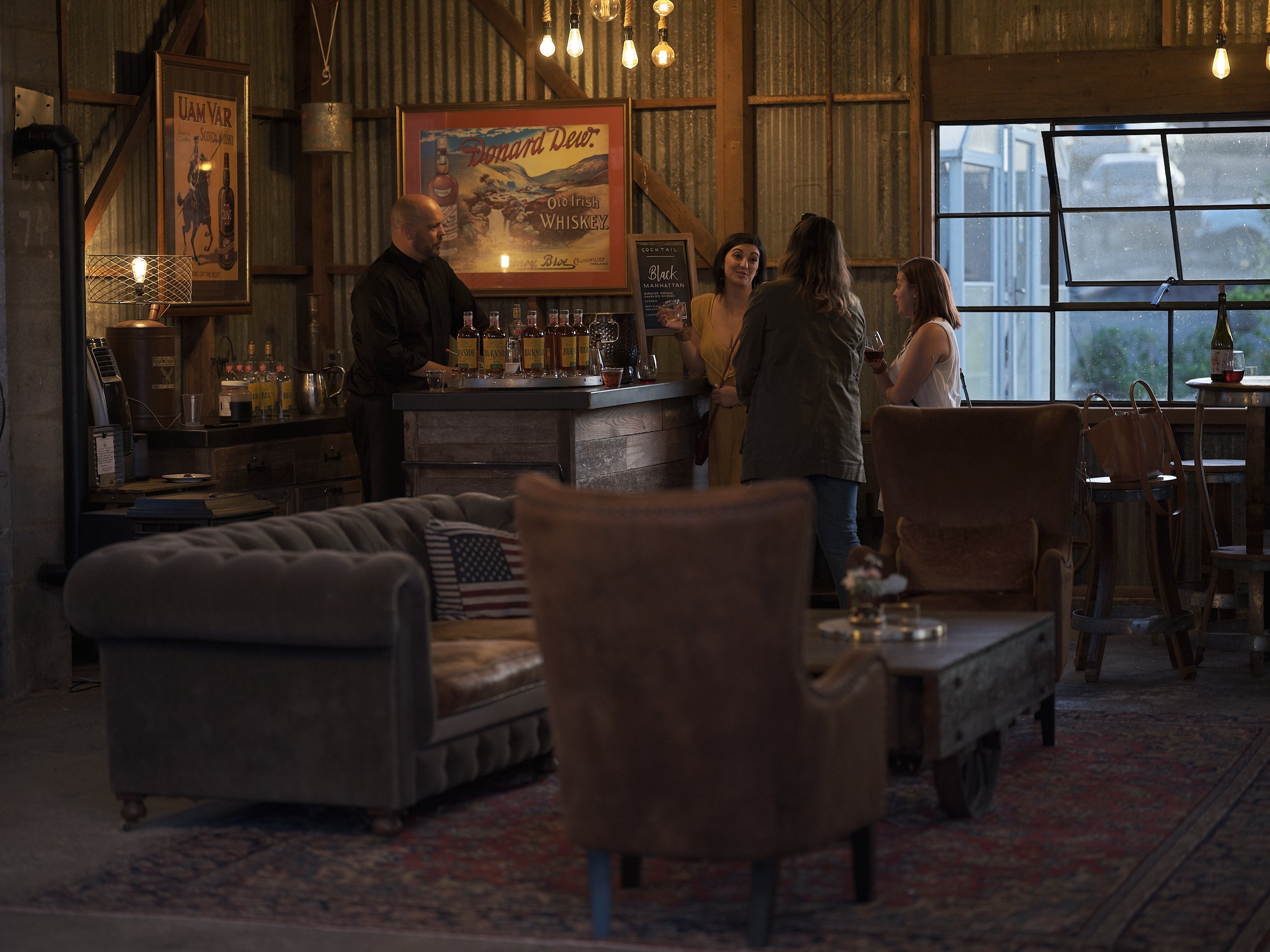 Customers are enjoying cocktails at a small craft cocktail bar in a converted barn.