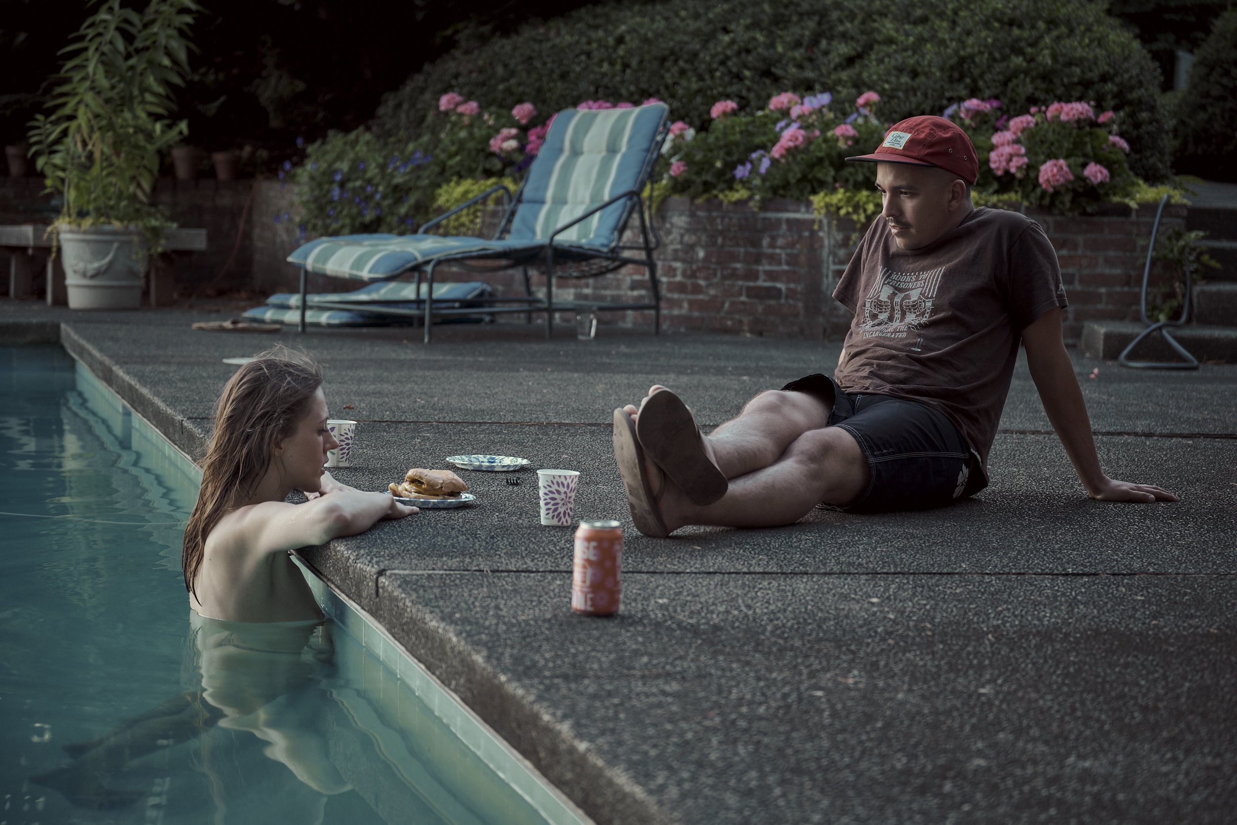 A woman, bathing in a swiming pool, is in thoughtful converstation with a man sitting nearby.