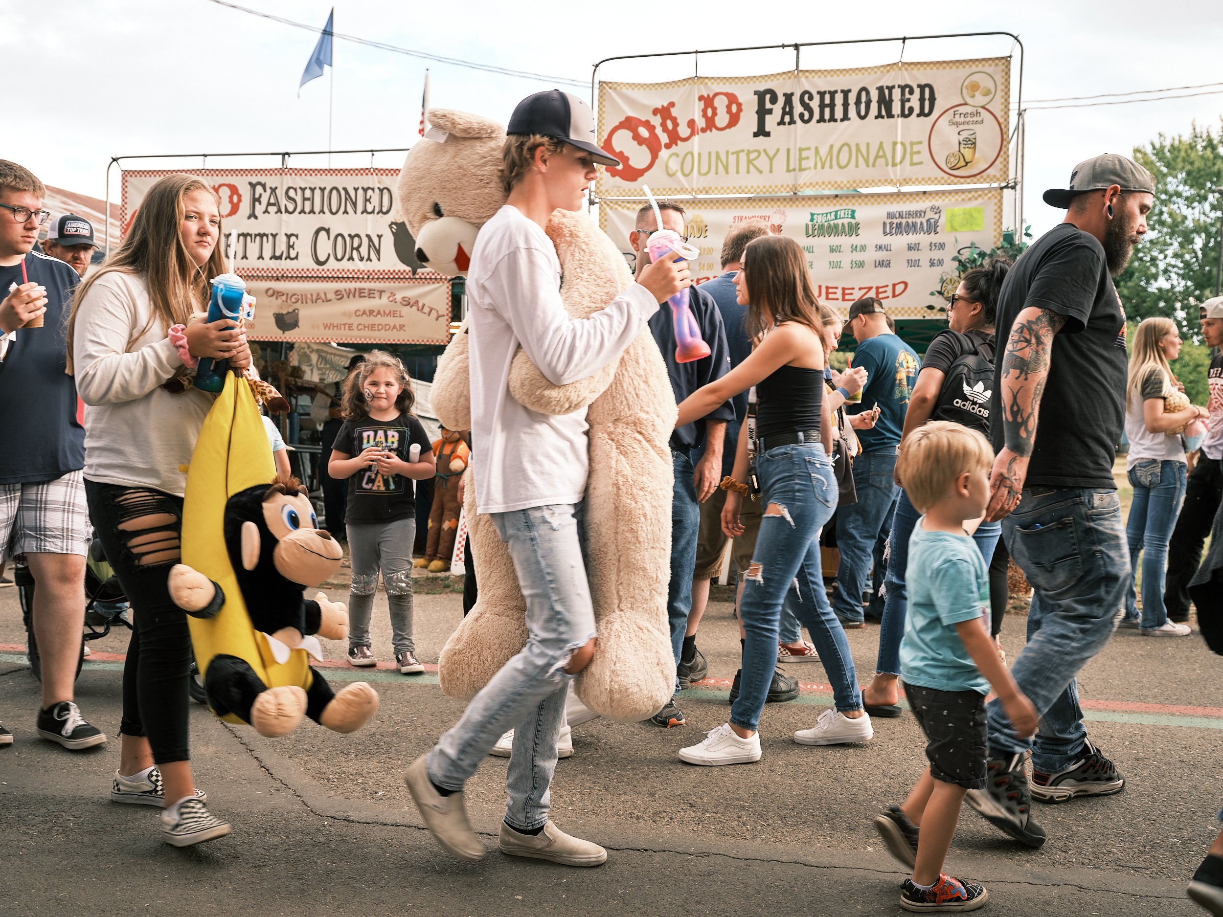 A crowd of county fair goers is passing by concession stands.