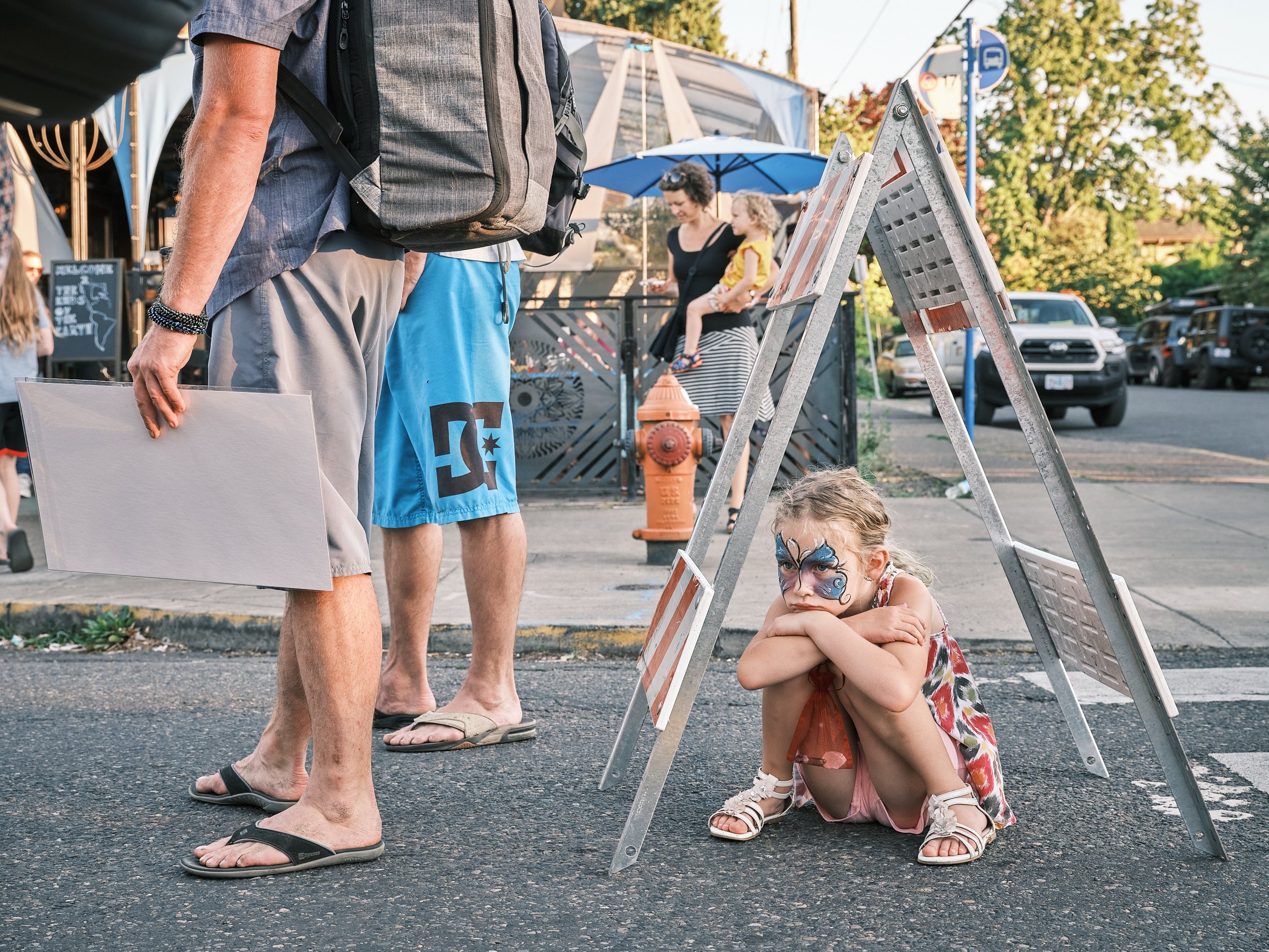 A sad looking girl sits under a street barricade at the Last Thursday Street Fair on Alberta Street in Portland, Oregon.