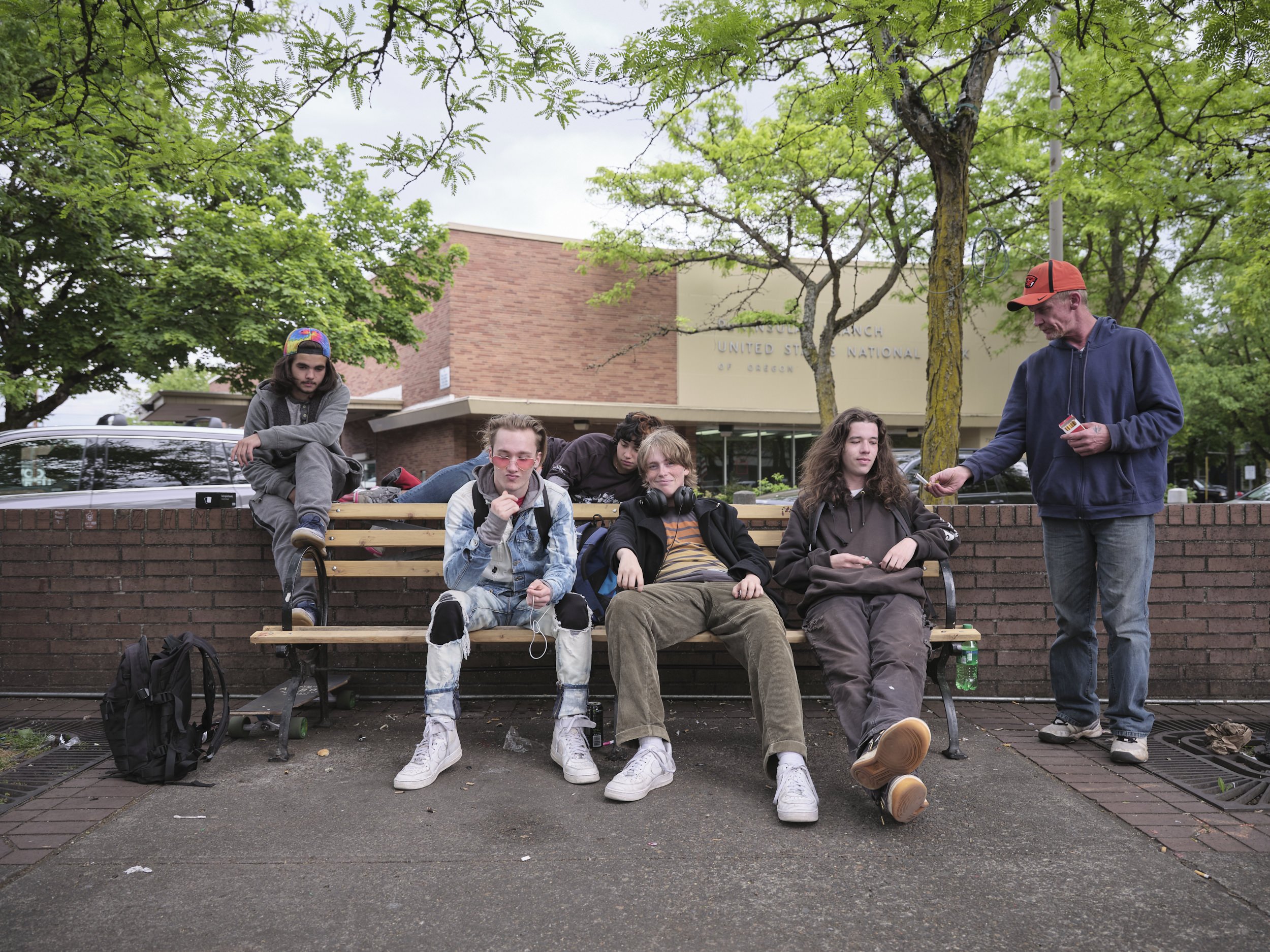 A group of teenagers is posing for a portrait while a middle aged man is offering them a cigarette.