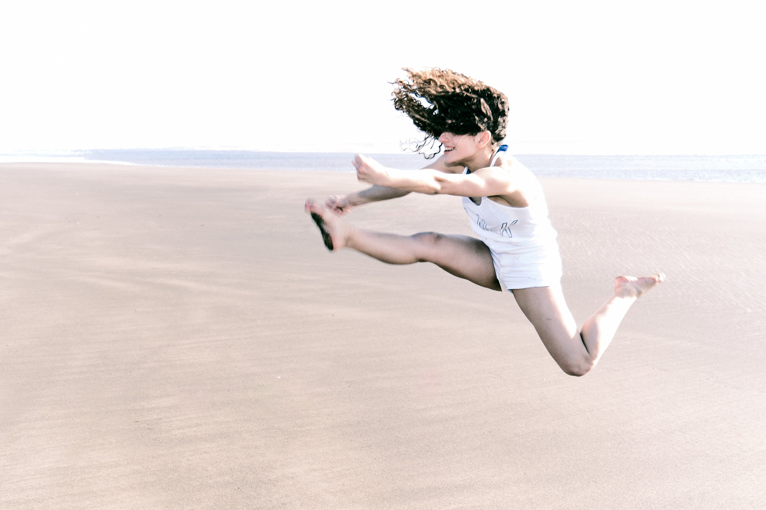 A young woman is jumping at the beach.