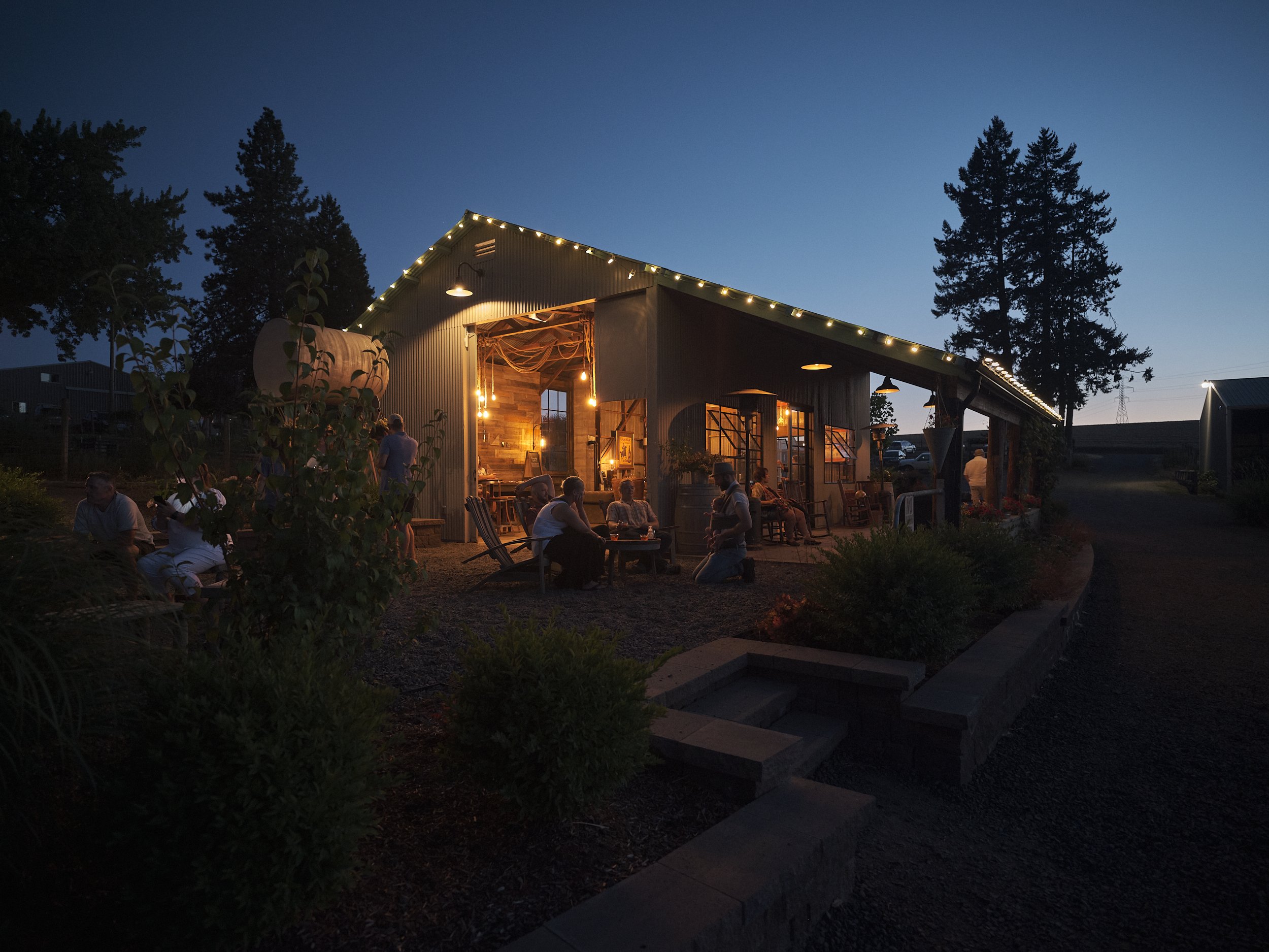 An exterior view of a barn at Abbey Road Farm and winery at dusk with guests enjoying the end of the day in Carlton, Oregon.