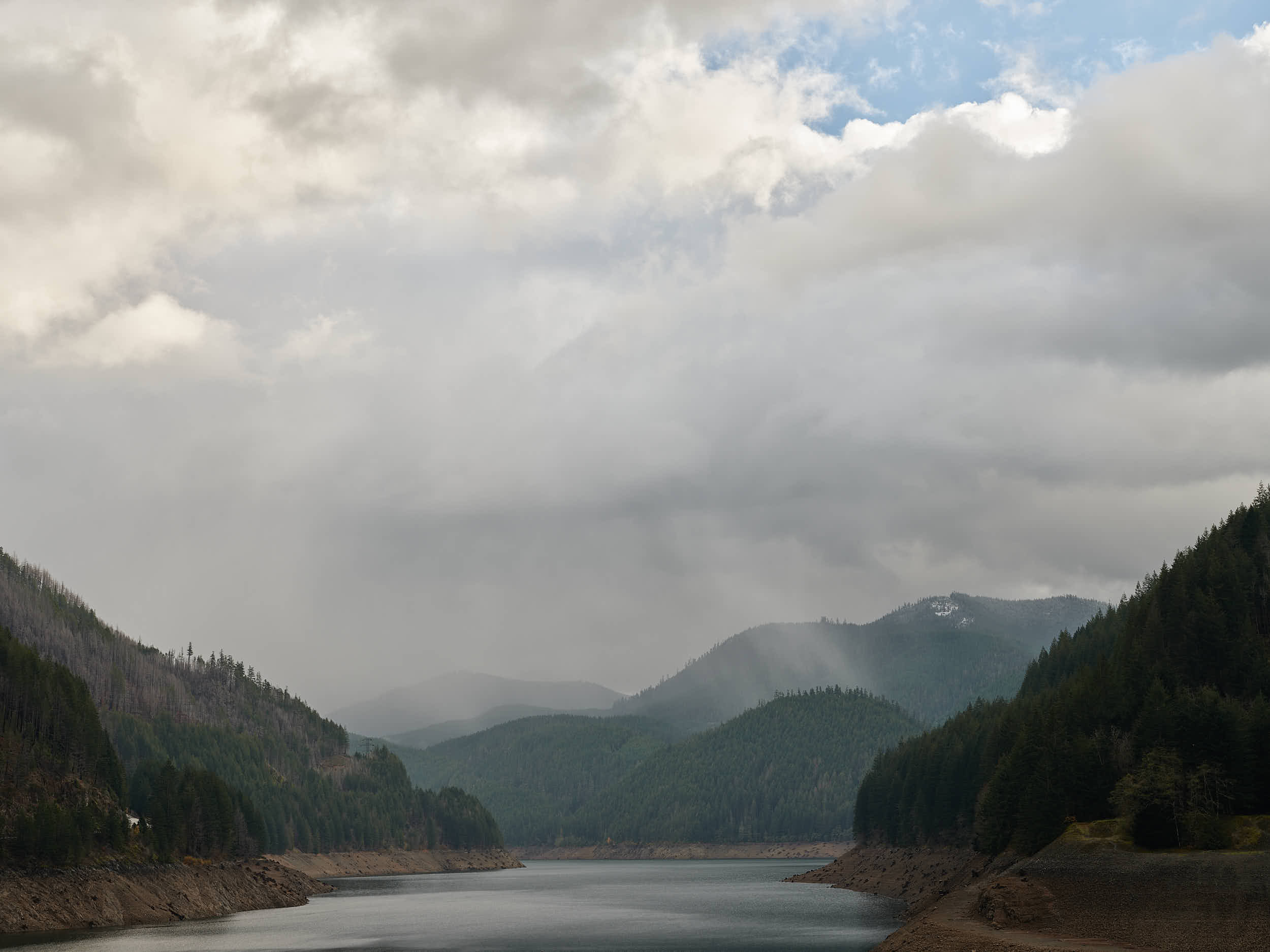 Detroit Lake in Oregon on a rainy winter day. Rain showers are visible in the distance.