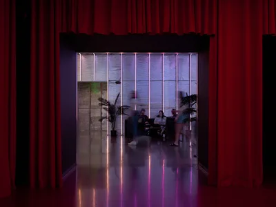 A contemporary restaurant interior at Hopscotch in Portland, Oregon featuring dramatic red curtains framing the entrance, purple and pink neon tube lighting, polished concrete floors with colorful reflections, and diners seated at tables in the background with decorative palm plants.