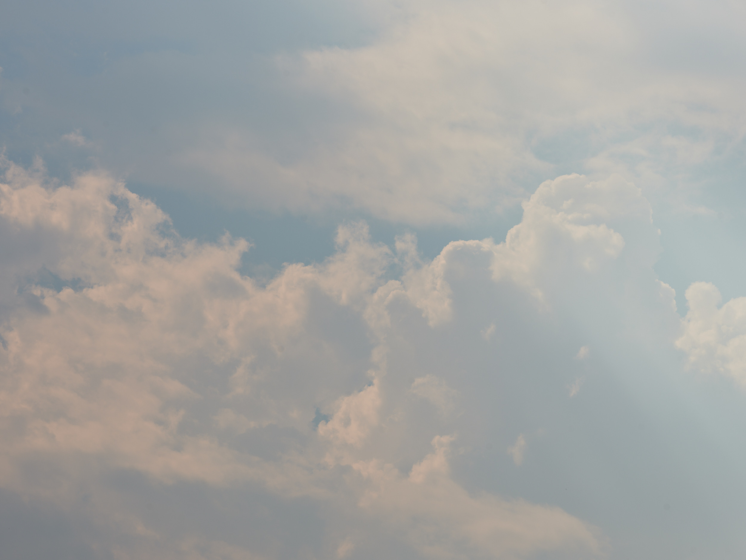 A dramatic sky filled with billowing white and gray cumulus clouds against a soft blue backdrop, captured over Portland, Oregon. The clouds create layers of depth and texture across the entire frame, suggesting changing weather conditions in the Pacific Northwest.
